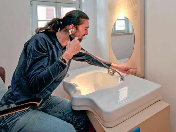 Ein Mann probiert die Hörstation zur sog. Haarschneideaktion in Pößneck von 1969 aus und sitzt dabei auf einem Friseurstuhl.